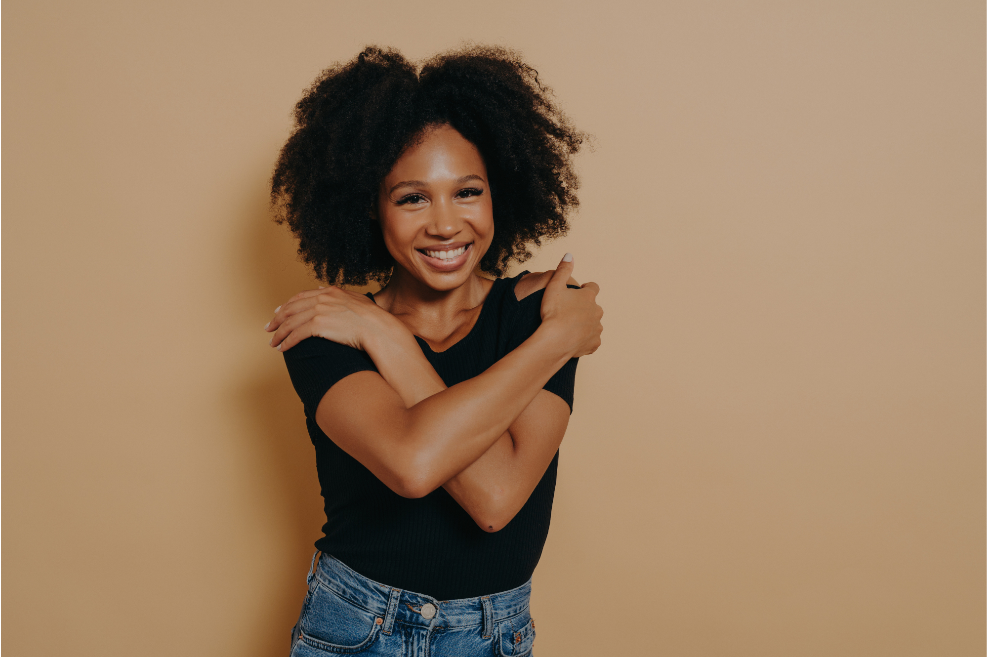 A Black woman is seen confidently demonstrating the "butterfly hug" that is commonly used as a method of Bilateral Stimulation in EMDR Therapy. The right hand is placed on the left shoulder, while the left is placed on the right, forming a cross over. Bilateral stimulation occurs with alternate tapping of either hand.